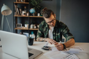 Tattooed hipster is using a calculator to sum all the bills