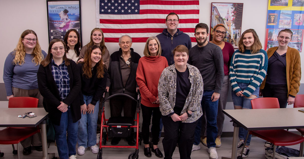 A group of people pose in front of an American flag
