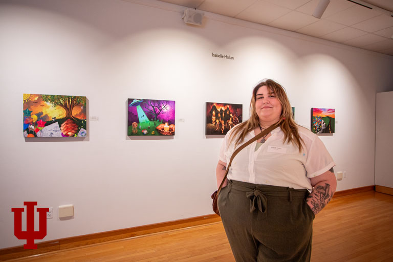 A woman stands in front of art work in a gallery
