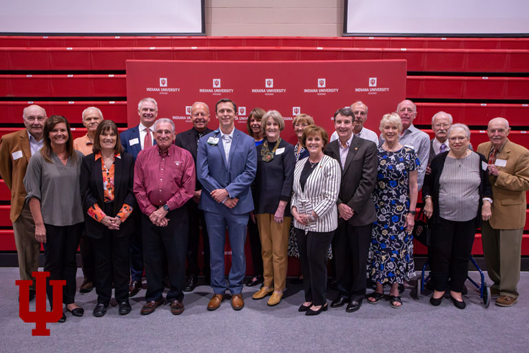 A group of people stand in front of a red background