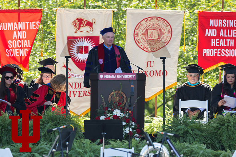 A man in academic regalia stands at a podium