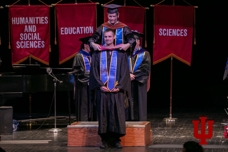 A man drapes an academic hood on a man standing on front of him