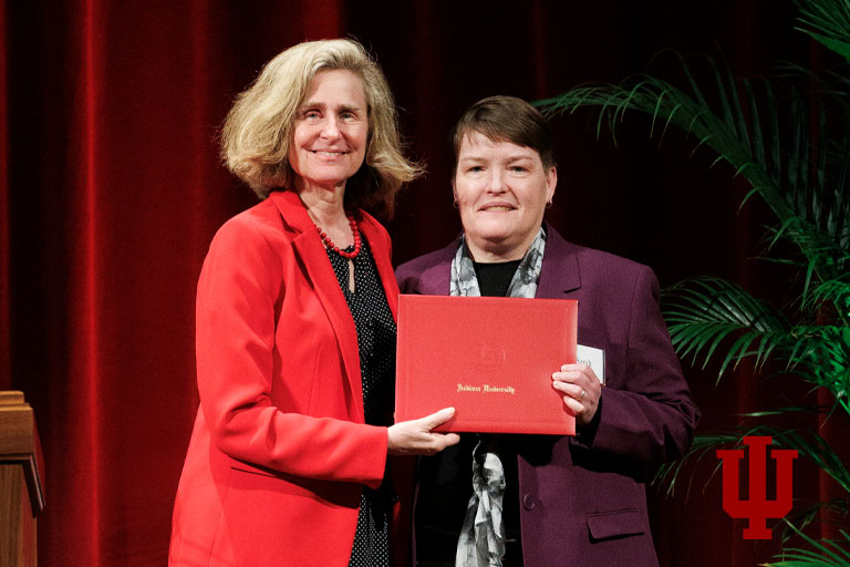 Two women stand holding an award