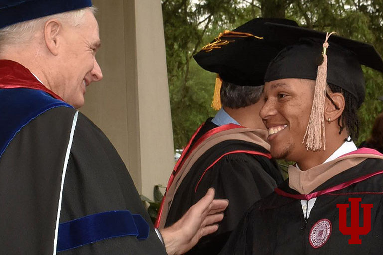 Two men in graduation regalia on a stage