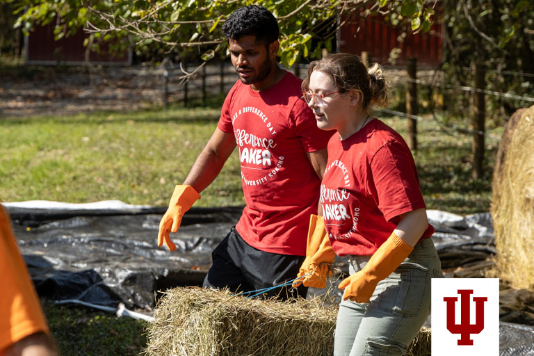 A man and a woman wearing red T-shirts carry a bale of hay