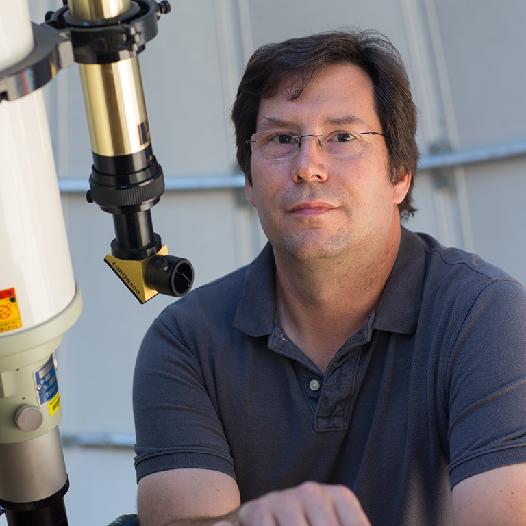 A man poses by a telescope