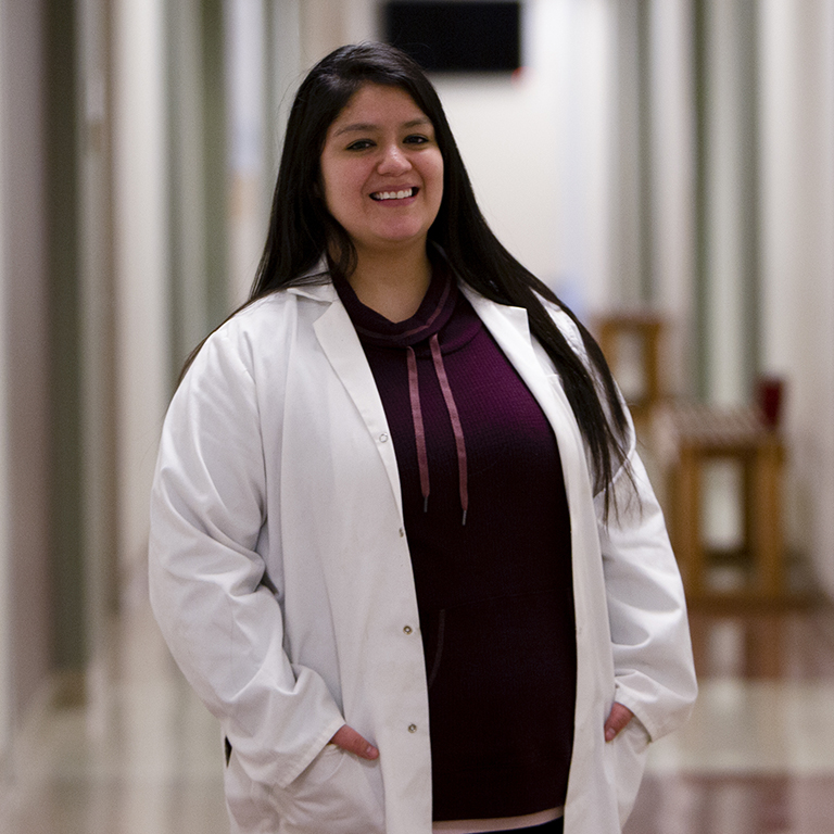 A woman poses in a white lab coat