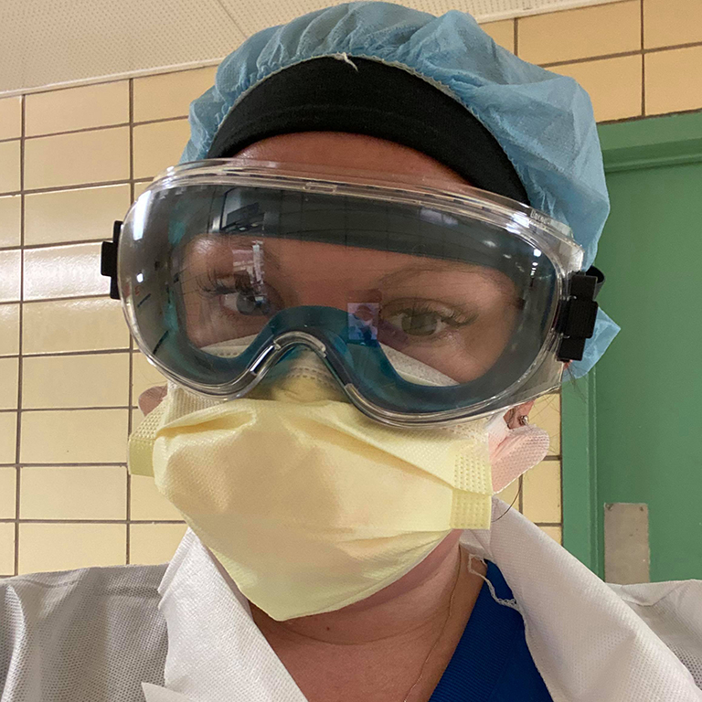 A woman wears a mask, surgical cap, and scrubs