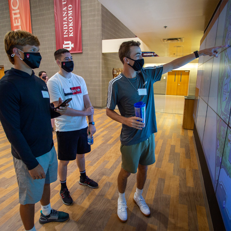 Three men in masks work in front of a computer wall