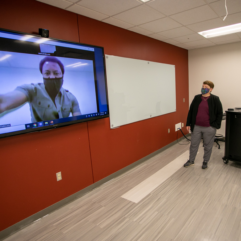 A man looks out of a large screen at a woman