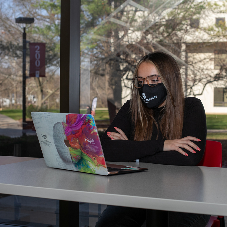 A woman sits in front of a laptop