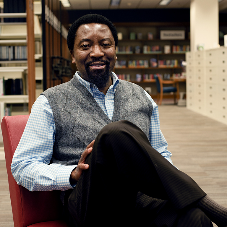 A man sits on a chair in a library.