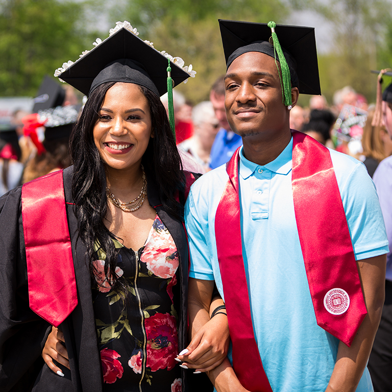 A woman and a man pose in graduation caps.