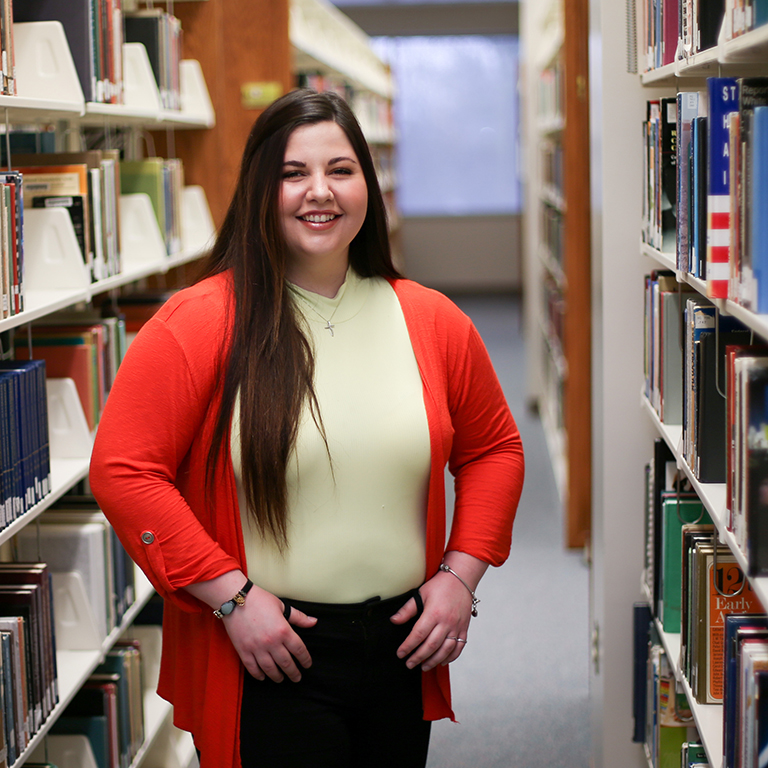 A woman poses between library shelves.