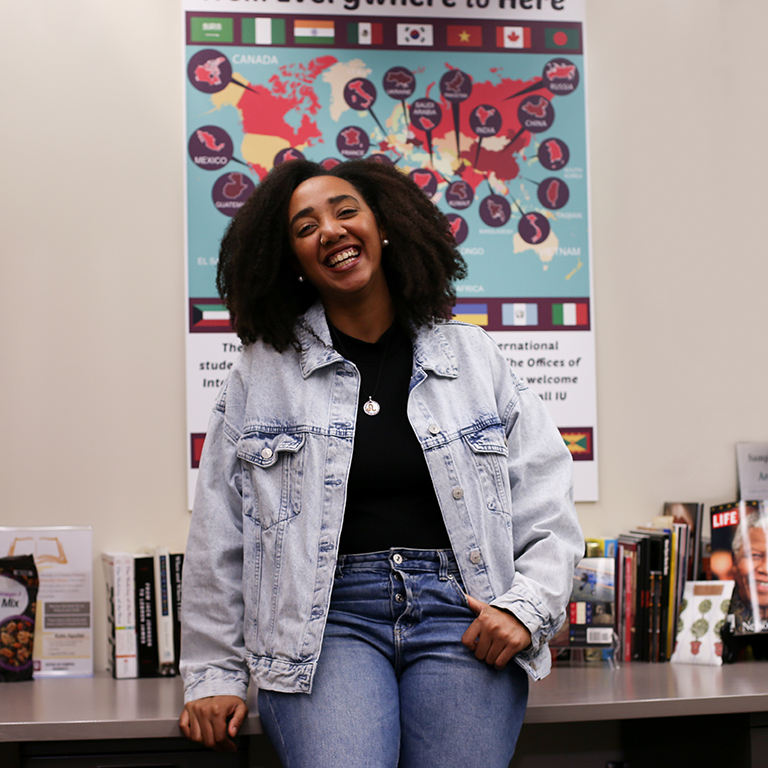 A smiling woman poses for a picture in front of a world map