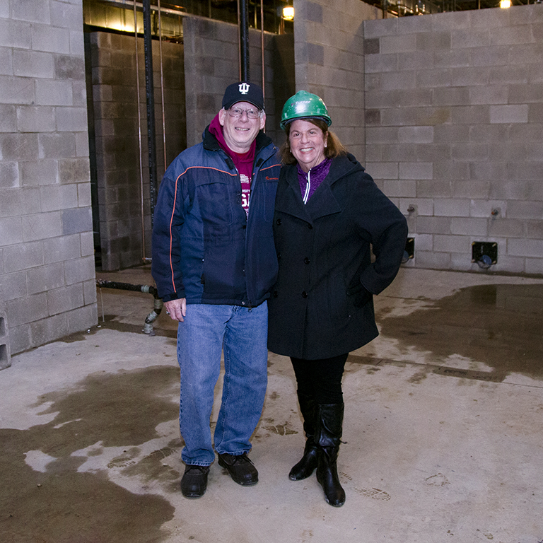 A man and a woman in hard hats pose in a construction site