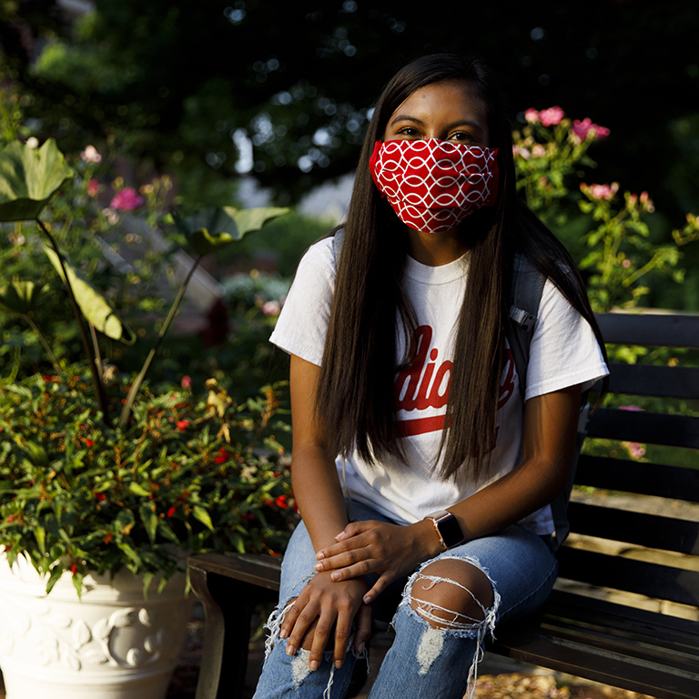 A woman wearing a red cloth mask sits on a bench