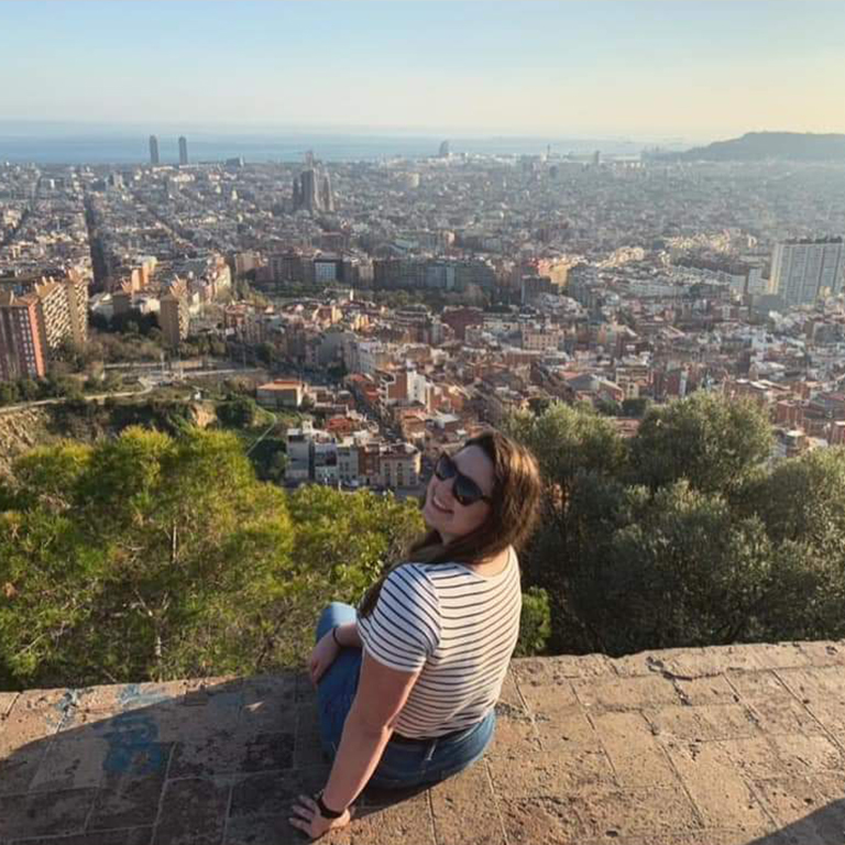 A woman sits on a wall overlooking a city
