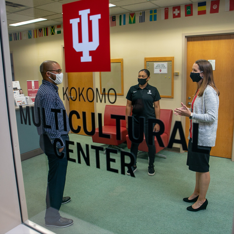 Three people talk behind a glass door with the words IU Kokomo Multicultural Center