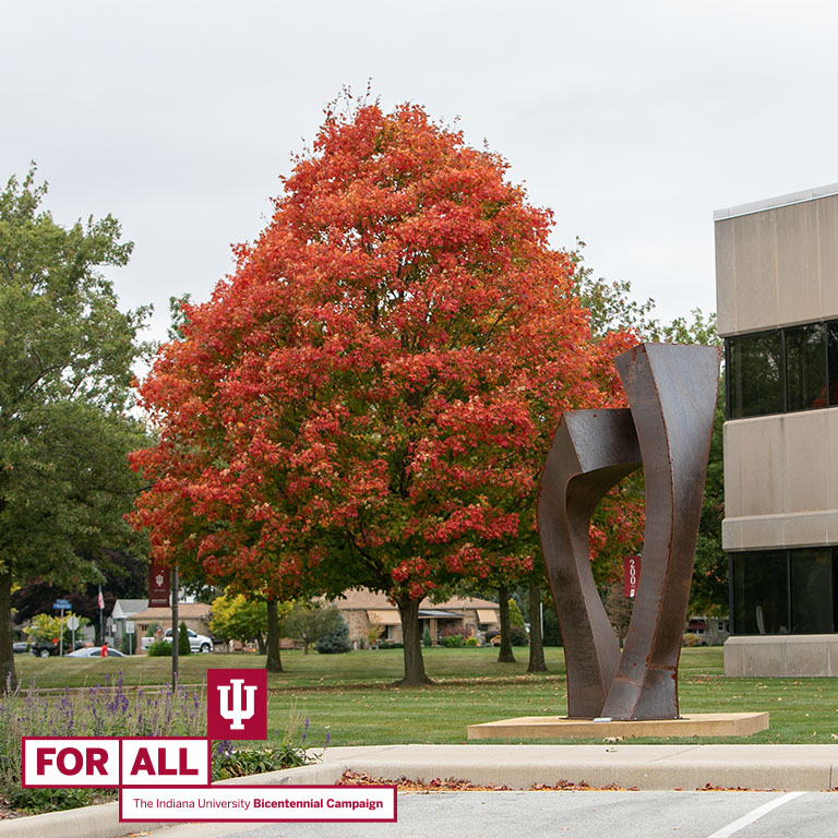 A tree with orange leaves behind a metal sculpture