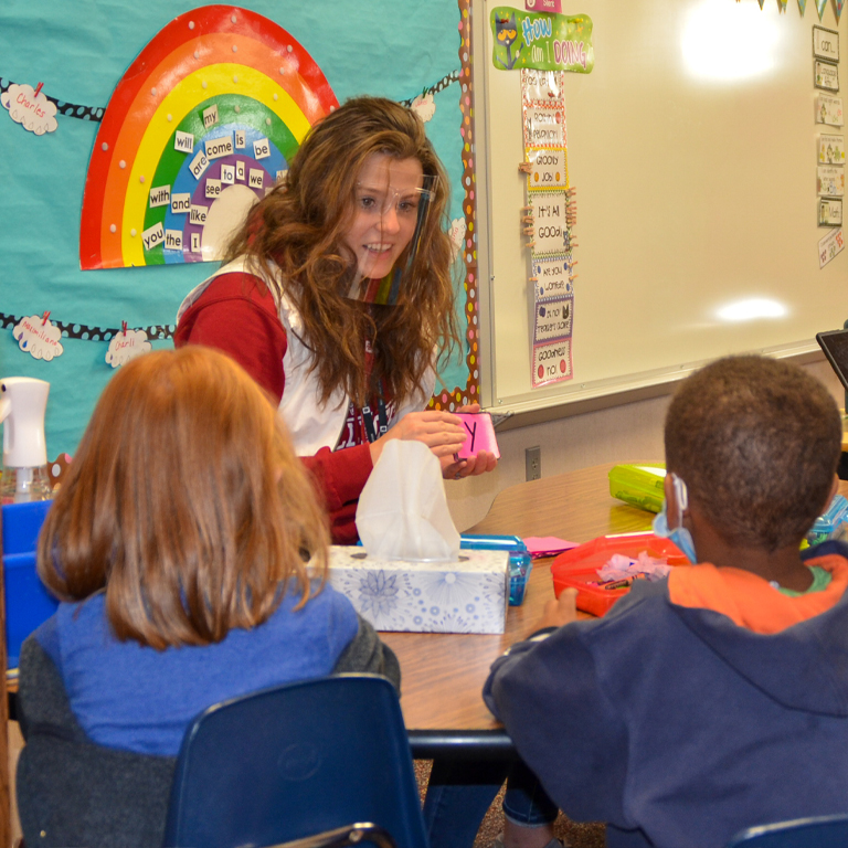 A woman holds a flash card seated in front of two children
