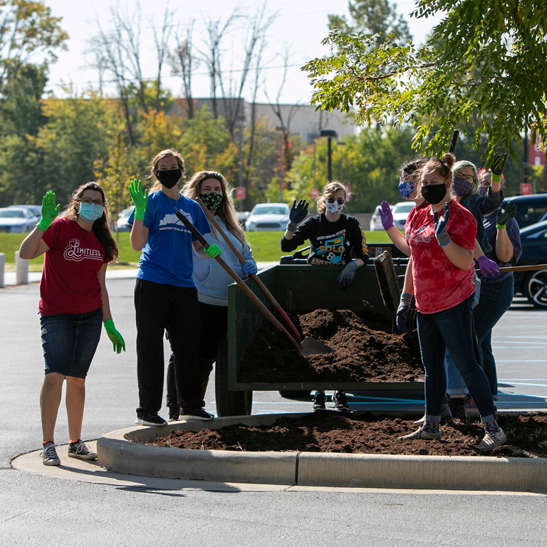 Seven people wave while shoveling mulch.