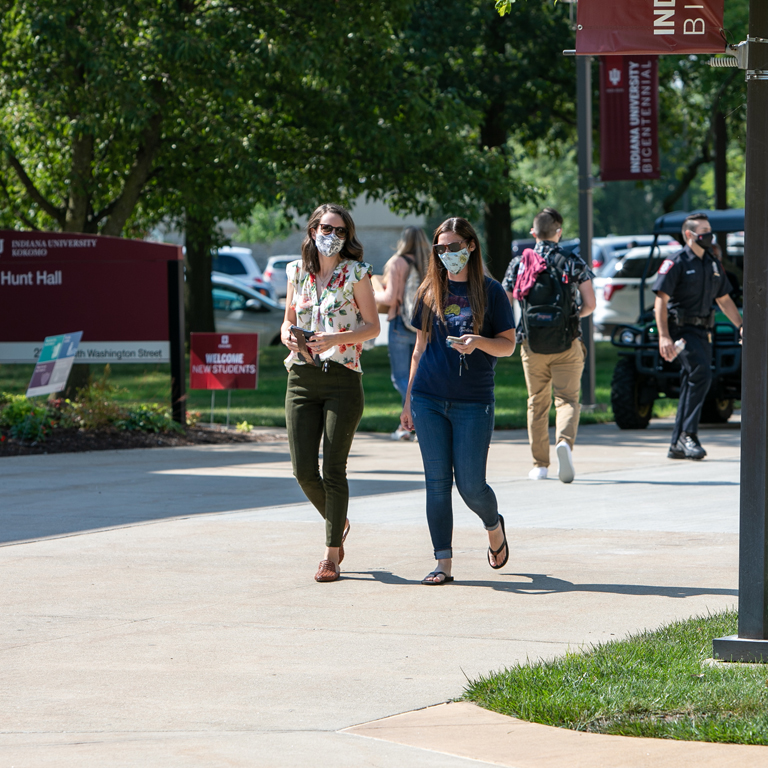 Two women in masks walk through the quad