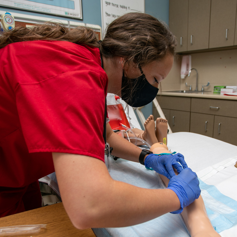 A woman in red scrubs places an IV in a virtual patient