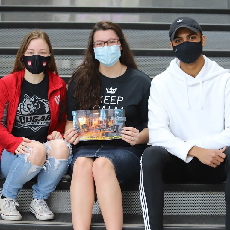 Three students set on steps with a map