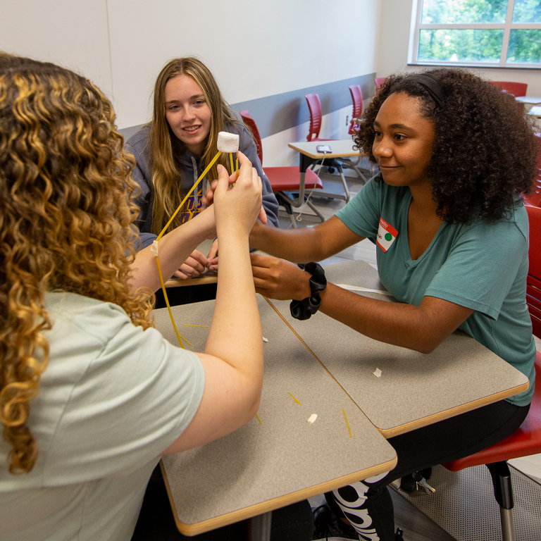 Three women build with noodles