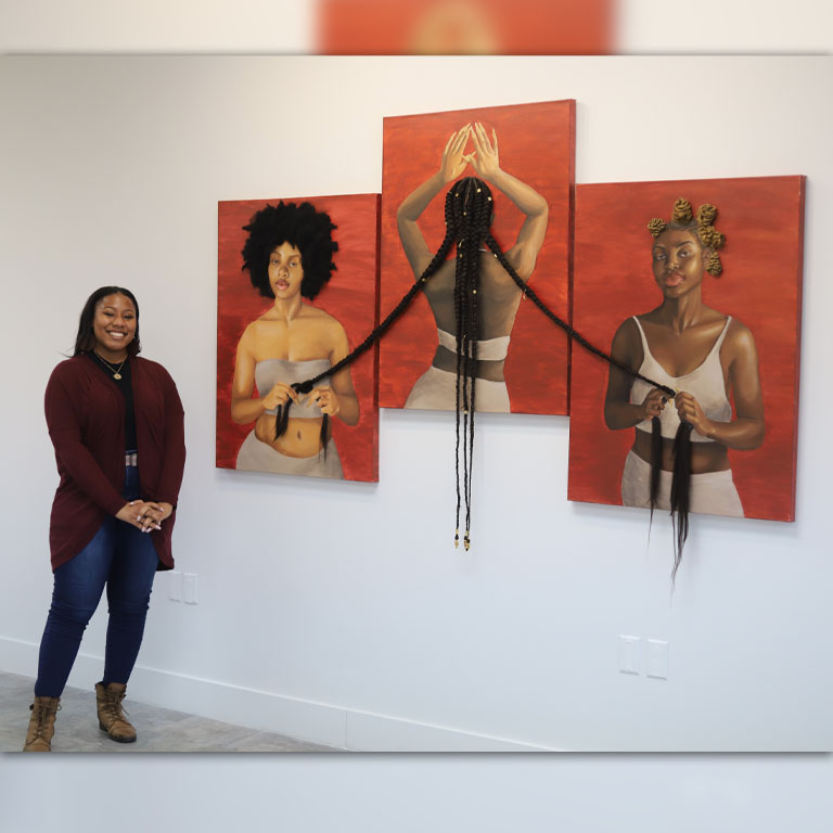 A woman stands in front of a three-paneled artwork