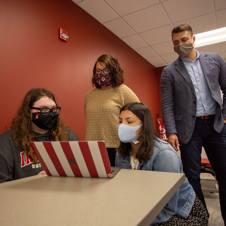Three women and a man look at a laptop screen