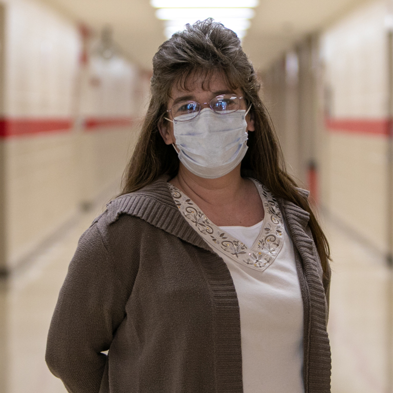 A woman in a mask stands in a high school hallway