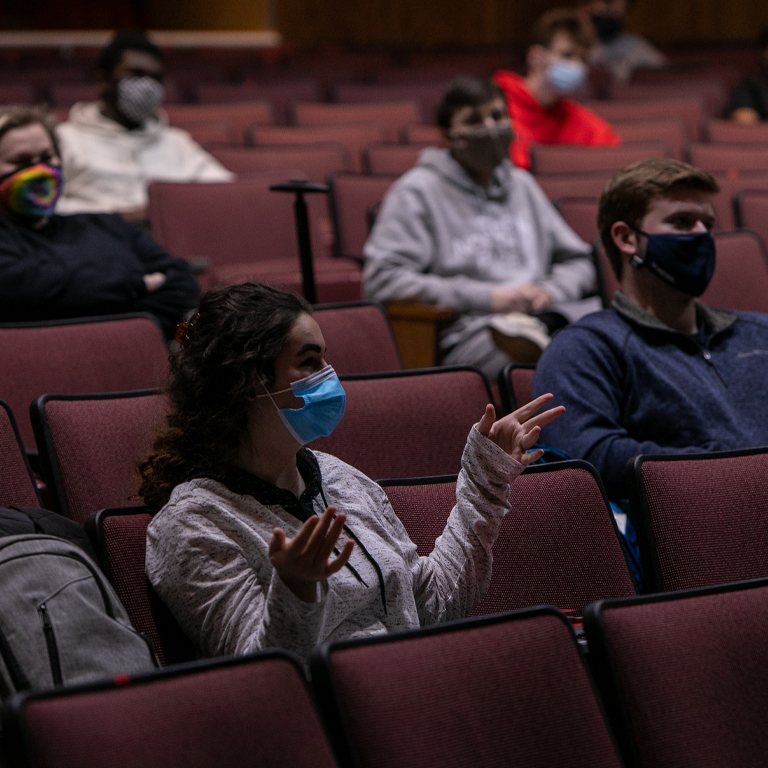 People in masks sit in an auditorium