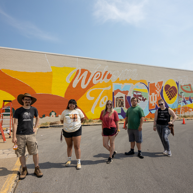 Two men and three women stand in front of a mural