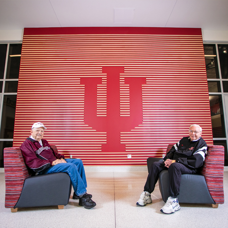 Two men sit in front of a red IU wall
