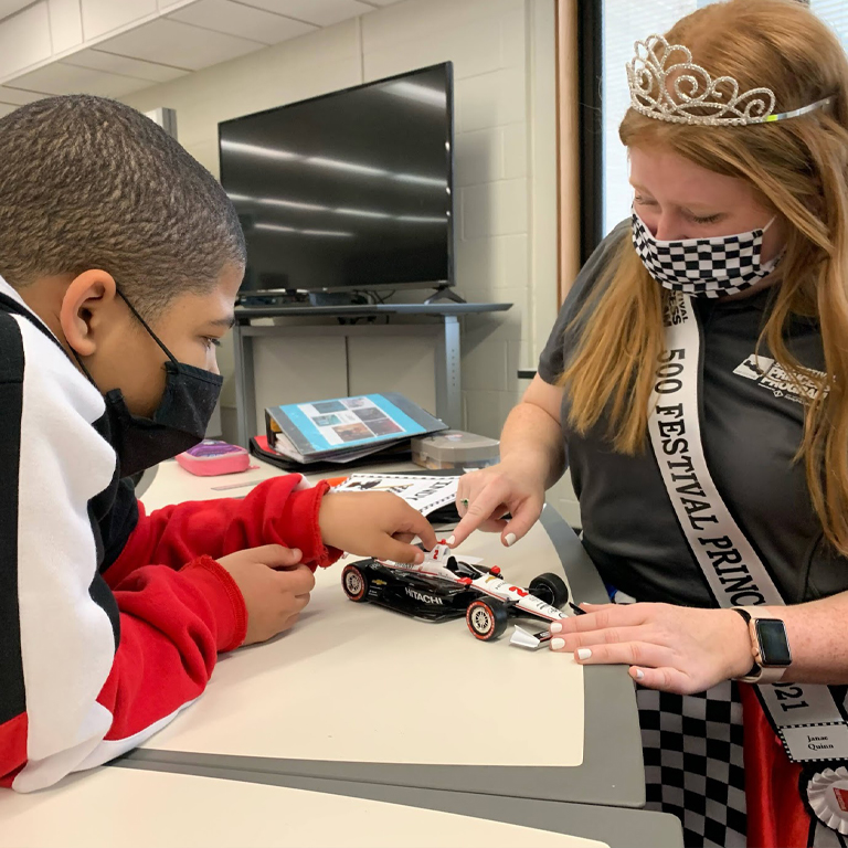 A woman in a crown and a boy look at a toy race car