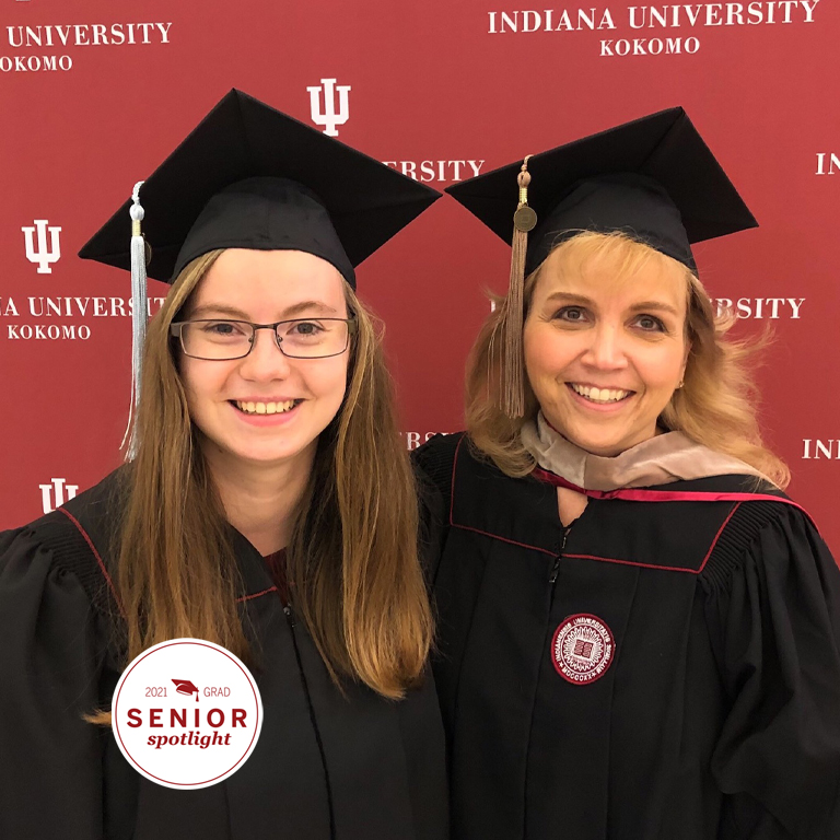 Two women in caps and grounds in front of a red backdrop