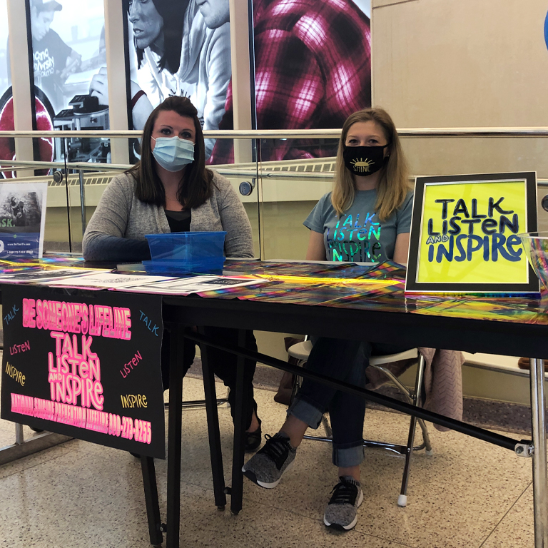 Two masked women sit behind a table