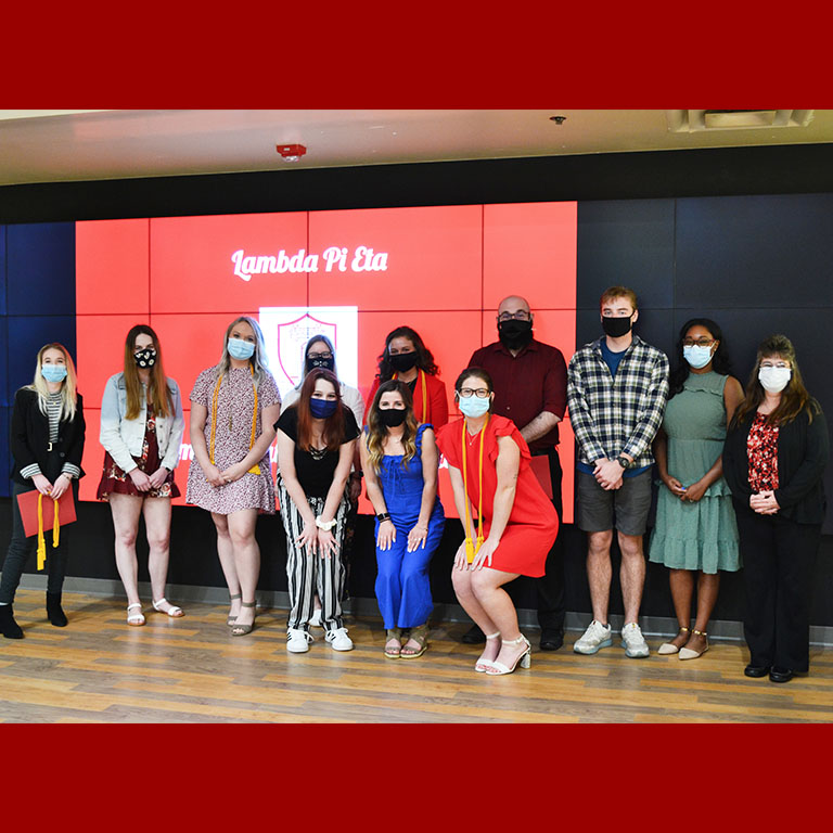 Twelve people wearing masks stand in front of a red screen