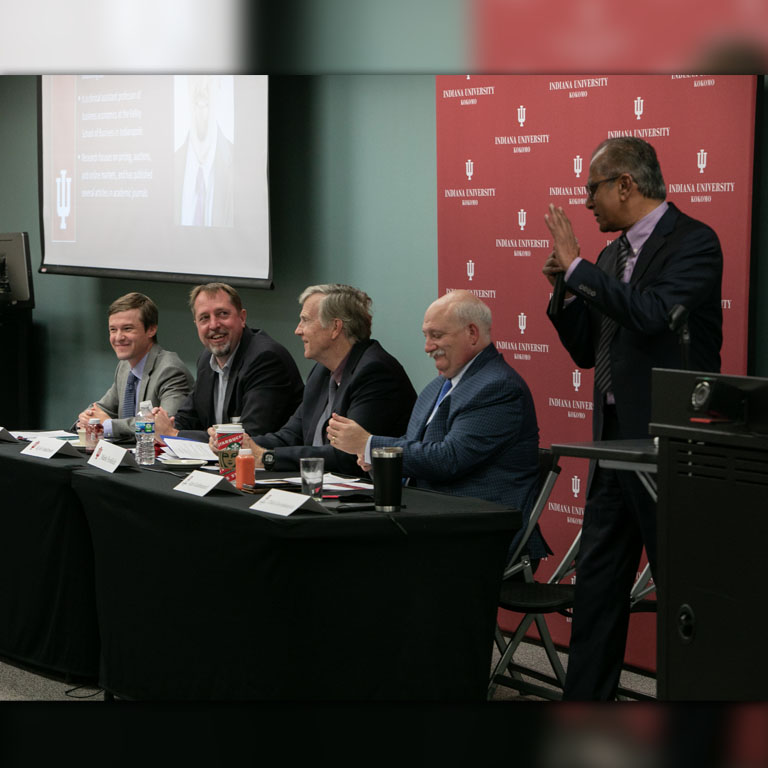 Five men sit or stand behind a table