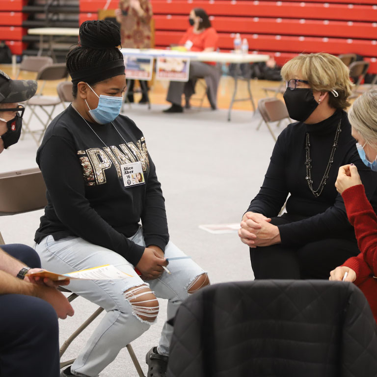 Three masked people sit in chairs in a circle