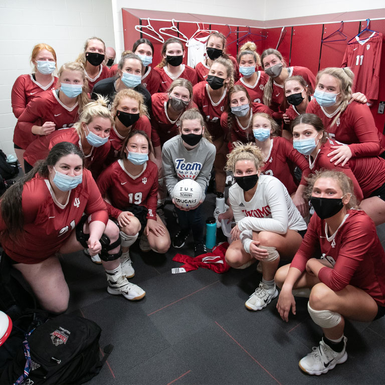 A group of college volleyball players in red gather around a teenager in gray