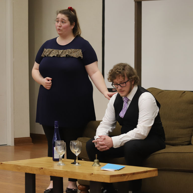Two students in a living room set for an opera
