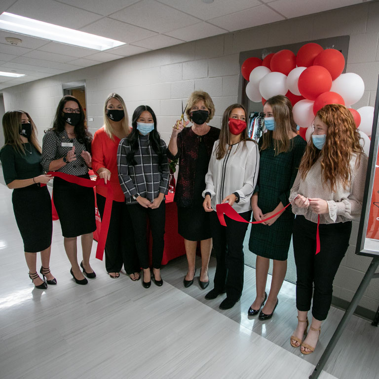 A group of eight women cut a red ribbon in front of a door