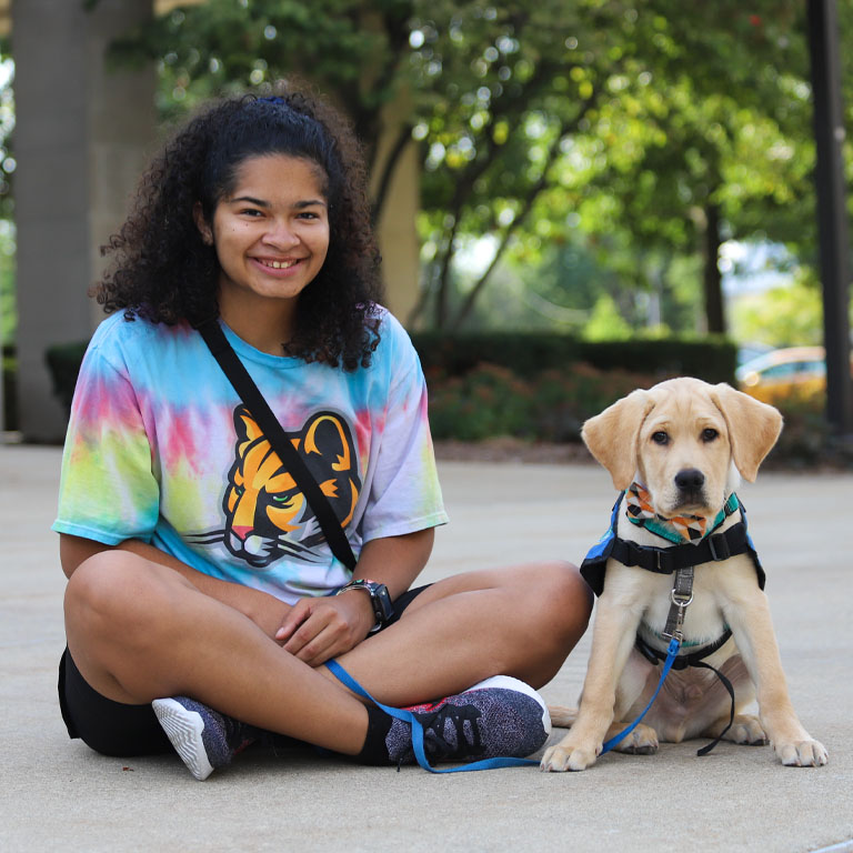 A woman sits with a service puppy in training
