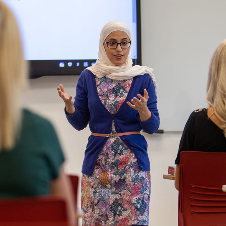 A woman in a hijab stands at the front of a classroom