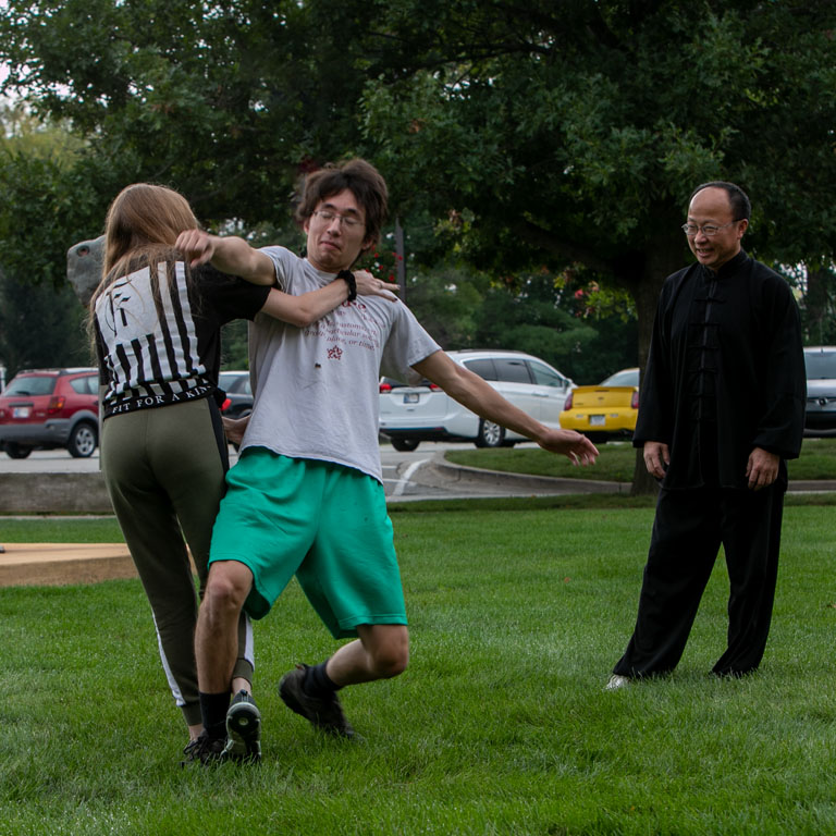 Two students practice self-defense techniques while the instructor watches