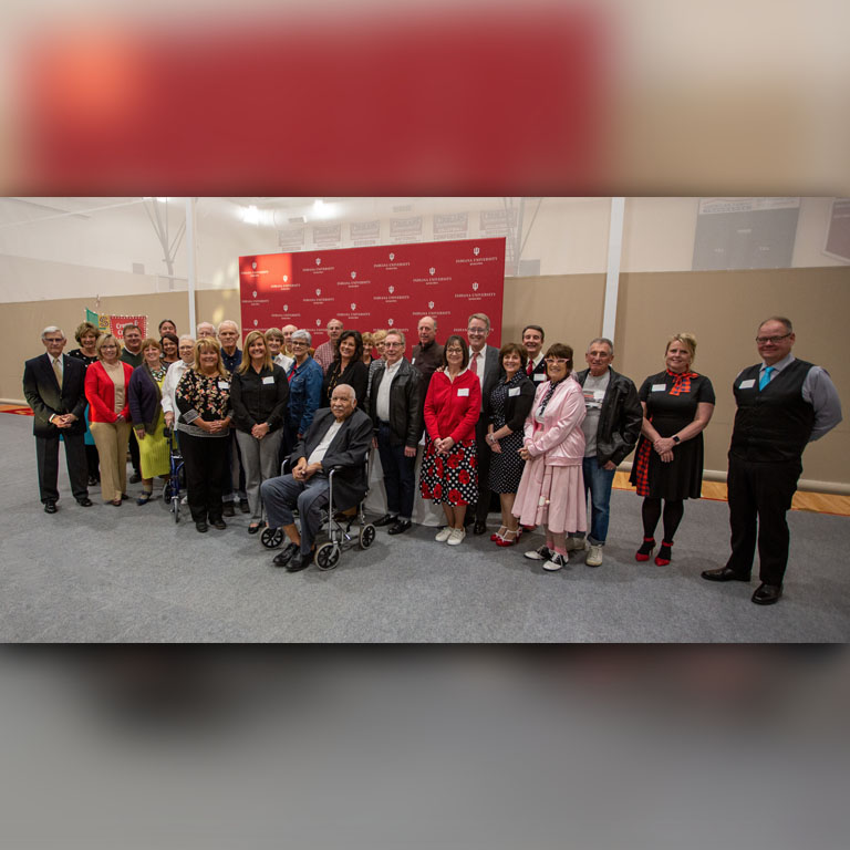 A large group of people pose in front of a red backdrop