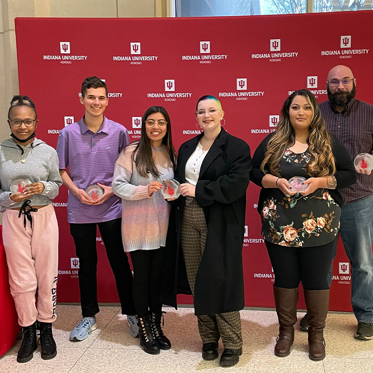 six people pose in front of a red backdrop